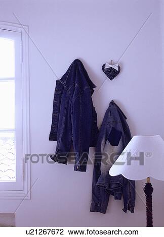 Stock Image - Close-up of blue denim jackets on hanging on white wall. Fotosearch