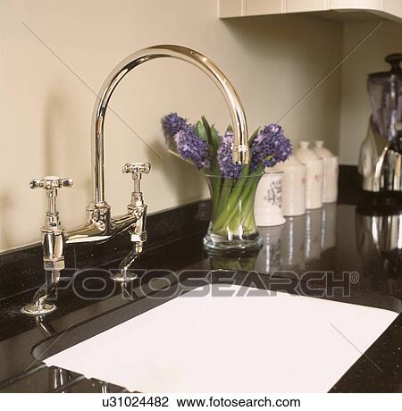 Stock Image - Close-up of chrome taps and white sink in black worktop. Fotosearch