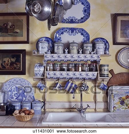Stock Image - Close-up of collection of blue+white china on shelves with matching trimming above white double sink. Fotosearch