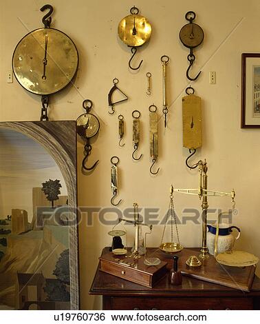 Stock Photograph - Close-up of collection of brass weighing scales on wall. Fotosearch
