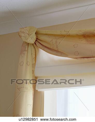 Stock Image - Close up of cream blind and swagged neutral curtains with script motif. Fotosearch
