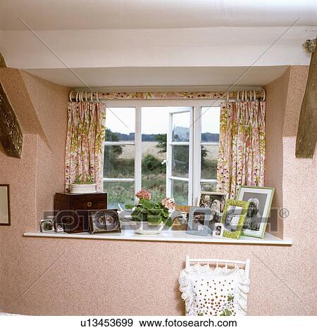 Stock Photo - Close-up of floral curtains with matching pole above casement window with photographs on windowsill. Fotosearch