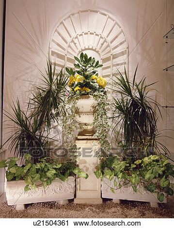 Stock Image - Close-up of group of houseplants in stone troughs and planters with large urn on a pedestal in the centre. Fotosearch