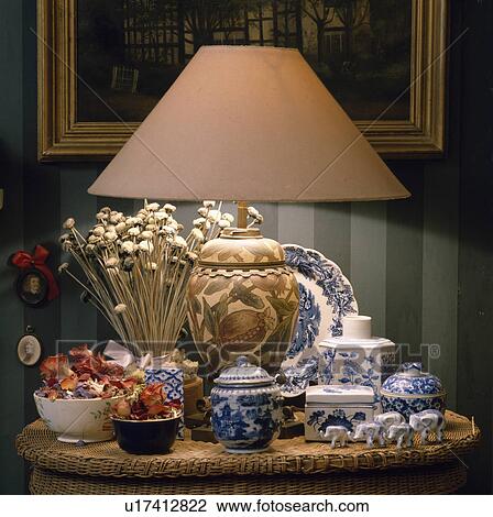 Stock Image - Close-up of lighted lamp on tablewith collection of blue+white china. Fotosearch