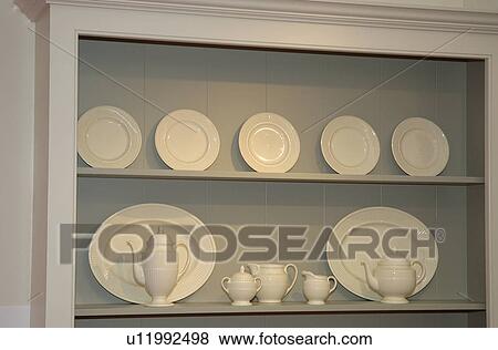 Stock Photo - Close-up of ream crockery with teapot and jugs on grey shelf unit. Fotosearch