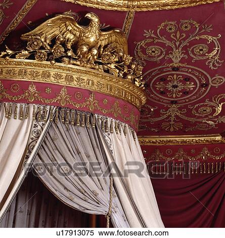 Stock Photography - Close-up of rococo ceiling and gilt coronet above bed drapes. Fotosearch