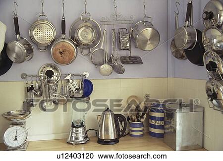 Stock Image - Close-up of stainless steel pans and utensils on hooks above electric blender and toaster on kitchen worktop. Fotosearch