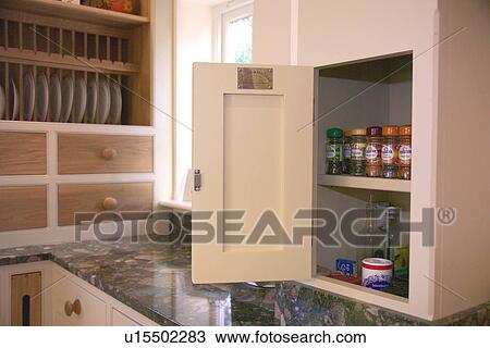Stock Image - Close-up of storage cupboard with open door and spice jars on shelves. Fotosearch