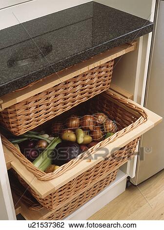 Stock Image - Close-up of vegetables in storage baskets below granite worktop. Fotosearch