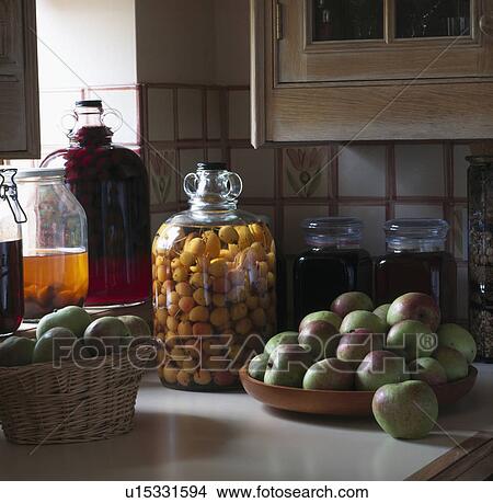 Picture - Closeup of apples in basket and dish on worktop with fruit in glass preserving jar. Fotosearch