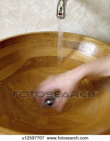 Stock Photo - Closeup of hand under tap in modern circular wooden basin. Fotosearch