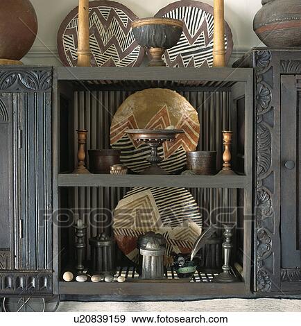 Stock Photo - Collection of African pottery and artefacts on carved wooden shelves. Fotosearch