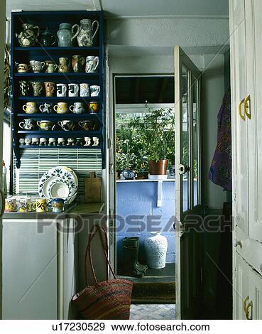 Stock Photo - Collection of pottery cups and jugs on shelves beside open kitchen door . Fotosearch