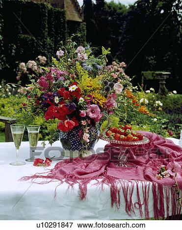 Stock Photo - Colourful fresh flowers in jug on white table cloth with pink shawl. Fotosearch