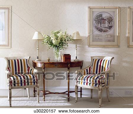 Colourful striped upholstered chairs on either side of antique console table below pictures in neutral hall View Large Photo Image Stock Photo - Colourful striped upholstered chairs on either side of antique console table below pictures in neutral hall. Fotosearch