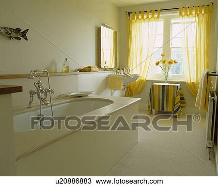 Stock Image - Contemporary white bathroom with stone top bath and yellow curtains. Fotosearch