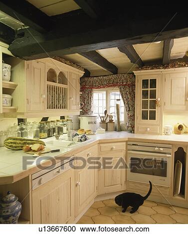 Corner of cream cottage kitchen with built-in dishwasher and oven and black cat on floor View Large Photo Image Stock Image - Corner of cream cottage kitchen with built-in dishwasher and oven and black cat on floor. Fotosearch