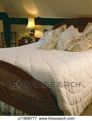 Cottage bedroom with lighted lamp beside bed with floral and lace-trimmed cushions and cream quilt View Large Photo Image Stock Photo - Cottage bedroom with lighted lamp beside bed with floral and lace-trimmed cushions and cream quilt. Fotosearch