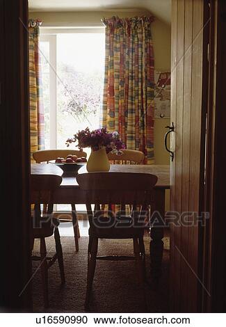 Stock Image - Cottage door open on to country dining room with pine table and chairs. Fotosearch
