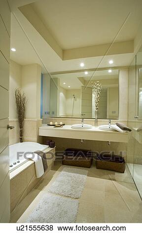 Stock Photo - Cream bathmats on floor of modern neutral bathroom with large mirror above vanity unit with built-in double basins. Fotosearch