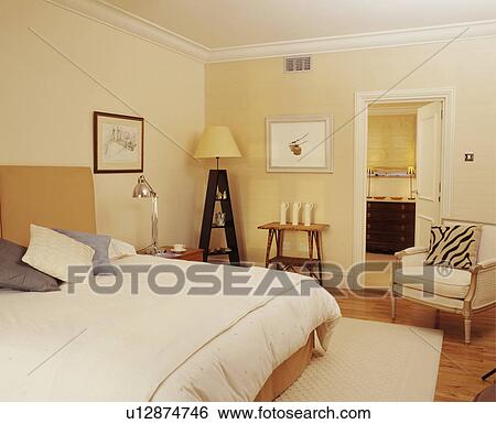 Cream bed cover on bed in modern bedroom with cream armchair beside door to ensuite bathroom View Large Photo Image Stock Photograph - Cream bed cover on bed in modern bedroom with cream armchair beside door to ensuite bathroom. Fotosearch