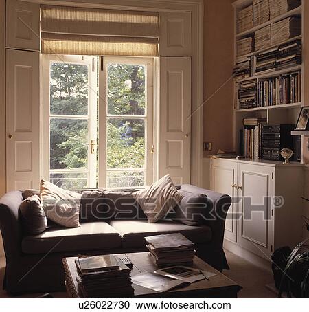 Stock Image - Cream blinds and shutters in traditional living room with neutral sofa. Fotosearch