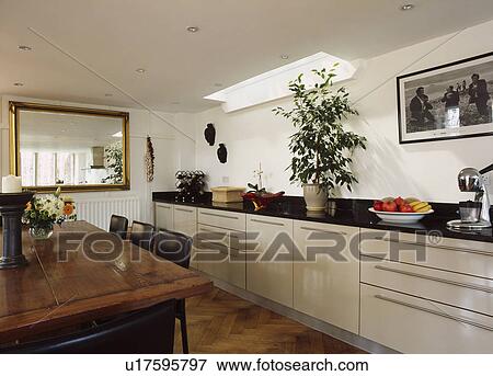Cream fitted cupboards in kitchen with parquet wood floor and large dining table with black leather chairs View Large Photo Image Stock Photo - Cream fitted cupboards in kitchen with parquet wood floor and large dining table with black leather chairs. Fotosearch