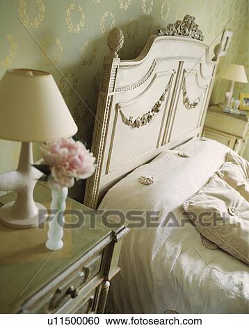 Cream Lamp And Pink Rose On Table Beside Cream French Bed With Cream Linen In Bedroom With Green Gold Wallpaper Stock Image