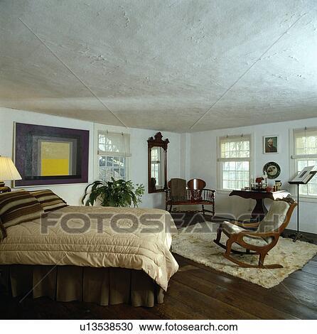 Cream quilt on bed in white country bedroom withrough-plastered ceiling and rocking chair on fur rug View Large Photo Image Stock Image - Cream quilt on bed in white country bedroom withrough-plastered ceiling and rocking chair on fur rug. Fotosearch