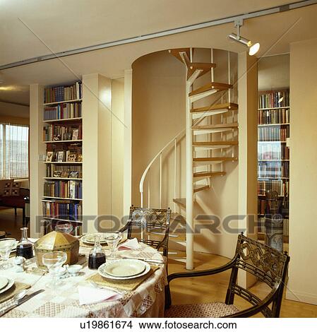 Picture - Cream spiral staircase in hall dining room with shelving and table set for dinner. Fotosearch