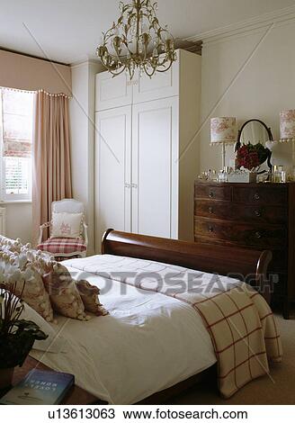 Stock Image - Cream wardrobe in bedroom with pink curtains and cream+red throw on mahogany bed . Fotosearch