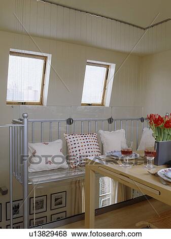Cushions on metal bench in attic conversion dining room with velux windows and pale wood table View Large Photo Image Stock Photo - Cushions on metal bench in attic conversion dining room with velux windows and pale wood table . Fotosearch