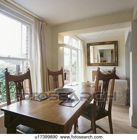 Stock Image - Dining room extension with cream curtains and pale wood table and chairs. Fotosearch