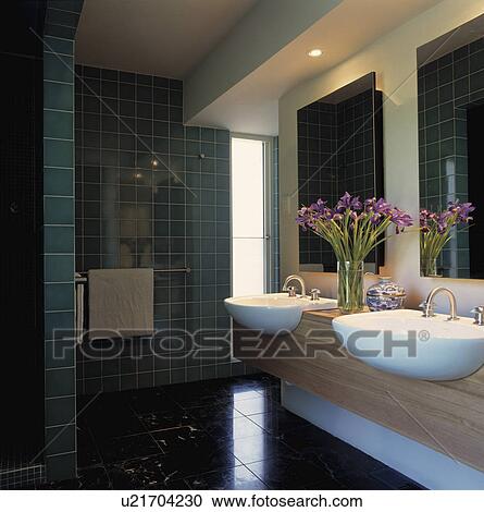 Stock Image - Double white basins in wooden vanity unit in modern bathroom with green wall tiles. Fotosearch