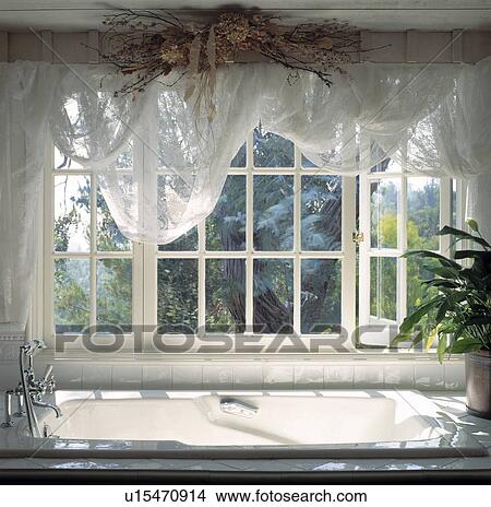 Dried flowers on beam above white voile drapes on window above white bath View Large Photo Image Picture - Dried flowers on beam above white voile drapes on window above white bath. Fotosearch