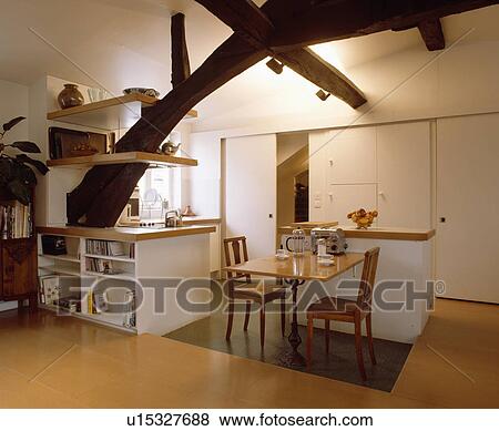 Fitted cupboard and shelves on large rustic beam in modern white attic kitchen with wooden chairs and table View Large Photo Image Stock Photo - Fitted cupboard and shelves on large rustic beam in modern white attic kitchen with wooden chairs and table. Fotosearch