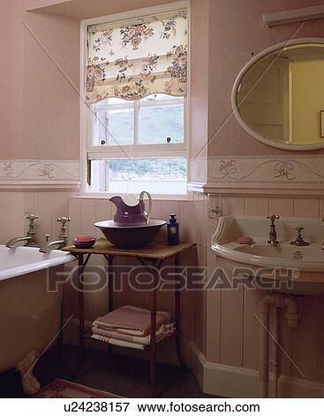 Stock Photo - Floral blind on window above small bambo table in pink bathroom with oval mirror above white basin . Fotosearch