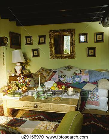 Stock Image - Floral cushions and patchwork quilt on sofa in pastel green cottage living room. Fotosearch