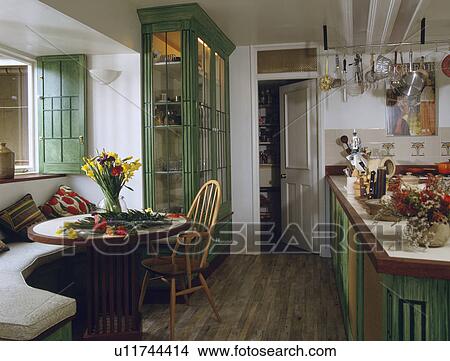 Flowers on circular table with banquette seating in white kitchen with green cupboard and wooden flooring View Large Photo Image Picture - Flowers on circular table with banquette seating in white kitchen with green cupboard and wooden flooring. Fotosearch