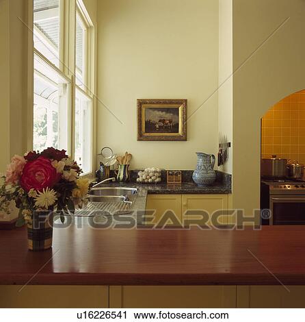 Stock Image - Flowers on wooden worktop in foreground of modern cream kitchen. Fotosearch