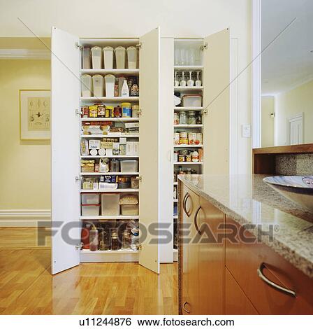 Fold Back White Doors On Floor To Ceiling Storage Shelves In Modern Kitchen Stock Photograph