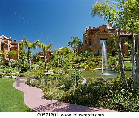 Fountain in pond and curved path in garden of newbuild Spanish holiday village View Large Photo Image Stock Image - Fountain in pond and curved path in garden of newbuild Spanish holiday village. Fotosearch