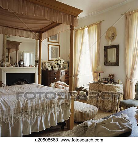 Four-poster pine bed with pink pelmet in traditional bedroom with cream curtains and floral-skirted dressing table View Large Photo Image Stock Photo - Four-poster pine bed with pink pelmet in traditional bedroom with cream curtains and floral-skirted dressing table. Fotosearch