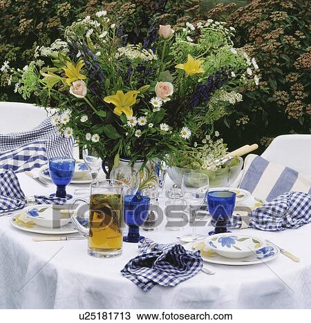 Stock Image - Fresh flowers and blue glasses on white tablecloth. Fotosearch