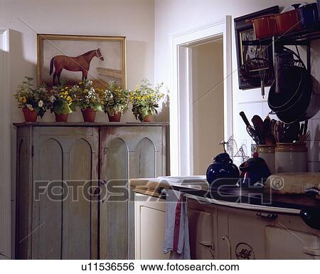 Stock Photograph - Fresh flowers in row of terracotta pots on grey distressed paint effect cupboard in cottage kitchen. Fotosearch