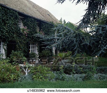 Stock Image - Furniture on patio in summer garden in front of country house. Fotosearch