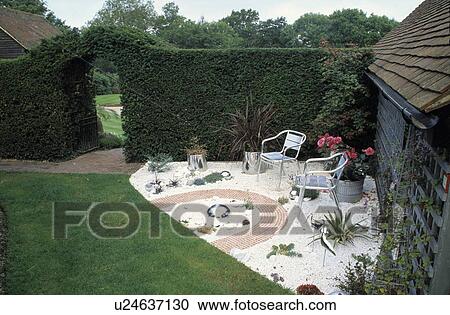 Stock Image - Furniture on patio in summer garden in front of country house. Fotosearch
