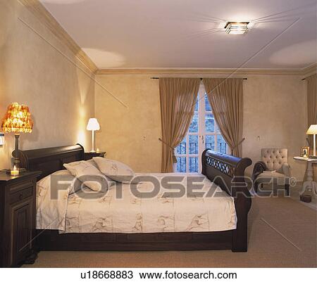 Stock Image - Giraffe-patterned bed linen on dark wood bed in neutral bedroom with sponge-effect walls and beige curtains. Fotosearch