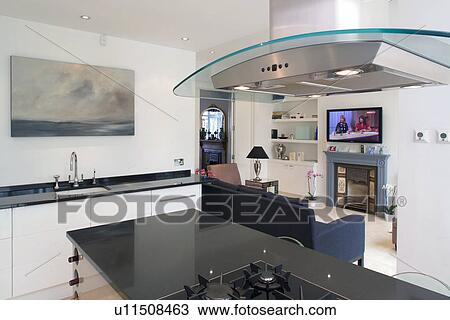 Glass and steel extractor above island unit in modern kitchen living room with flatscreen TV above fireplace View Large Photo Image Stock Image - Glass and steel extractor above island unit in modern kitchen living room with flatscreen TV above fireplace. Fotosearch