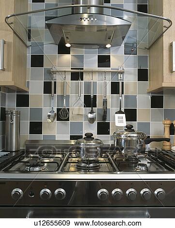 Glass and steel extractor fan above hob and range oven below grey and black tiled splashback View Large Photo Image Stock Photo - Glass and steel extractor fan above hob and range oven below grey and black tiled splashback. Fotosearch
